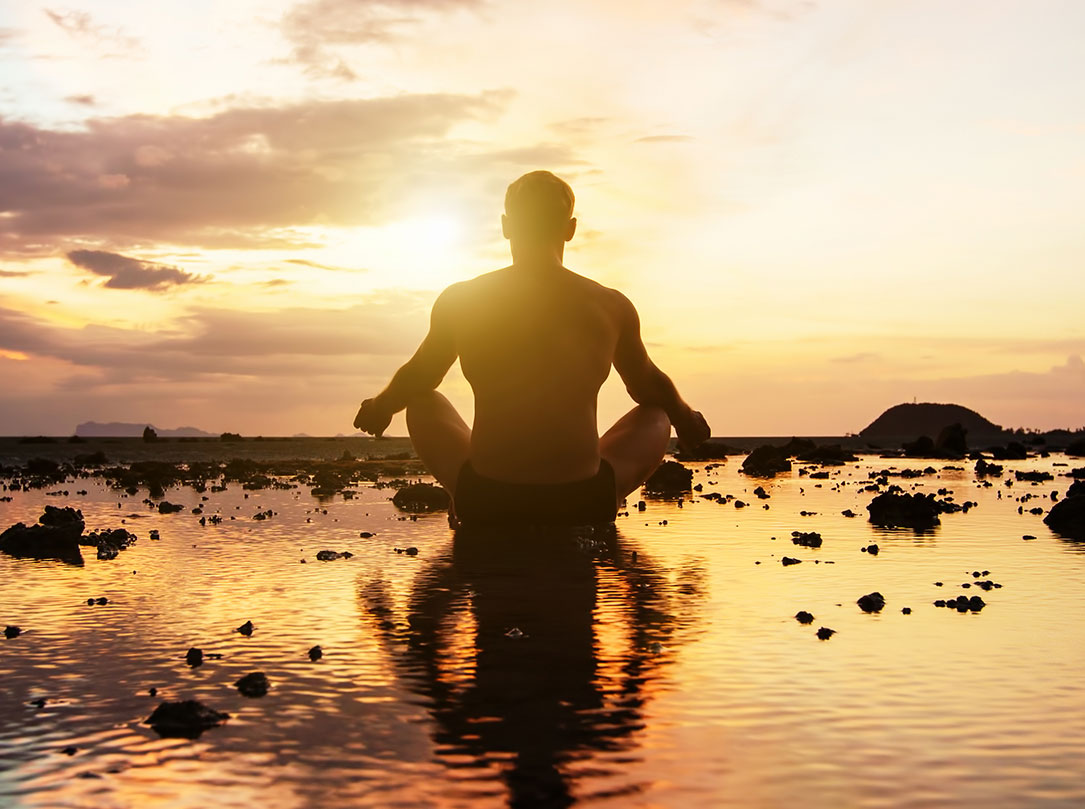 Silhouette of man in sitting yoga pose facing the sunset