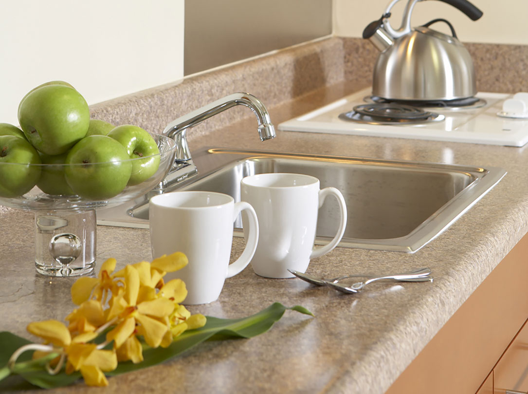 Kitchen counter with sink, stove top, 2 white mugs and bowl of green apples