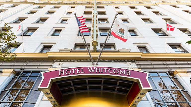 Hotel Whitcomb Exterior front view, with hotel Whitcomb name board having two flags placed on top of the board.